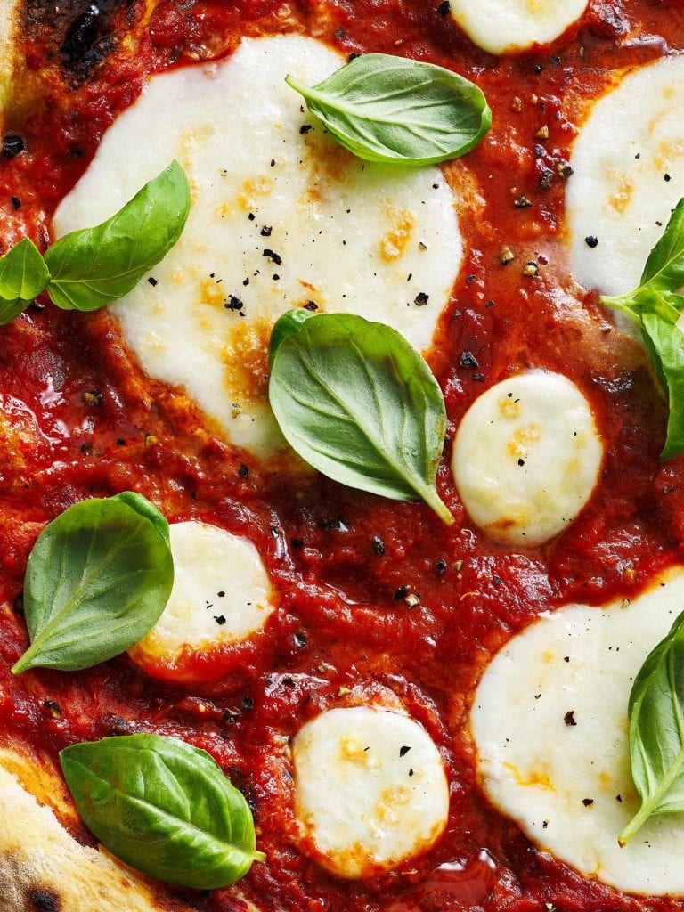 macro food photography of mozzarella pizza garnished with basil leaves