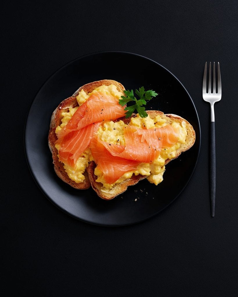 Shot for Marks and Spencer Hospitality Menus. Scrambled eggs and smoked salmon on toast. Graphic image shot on black plate with black background.