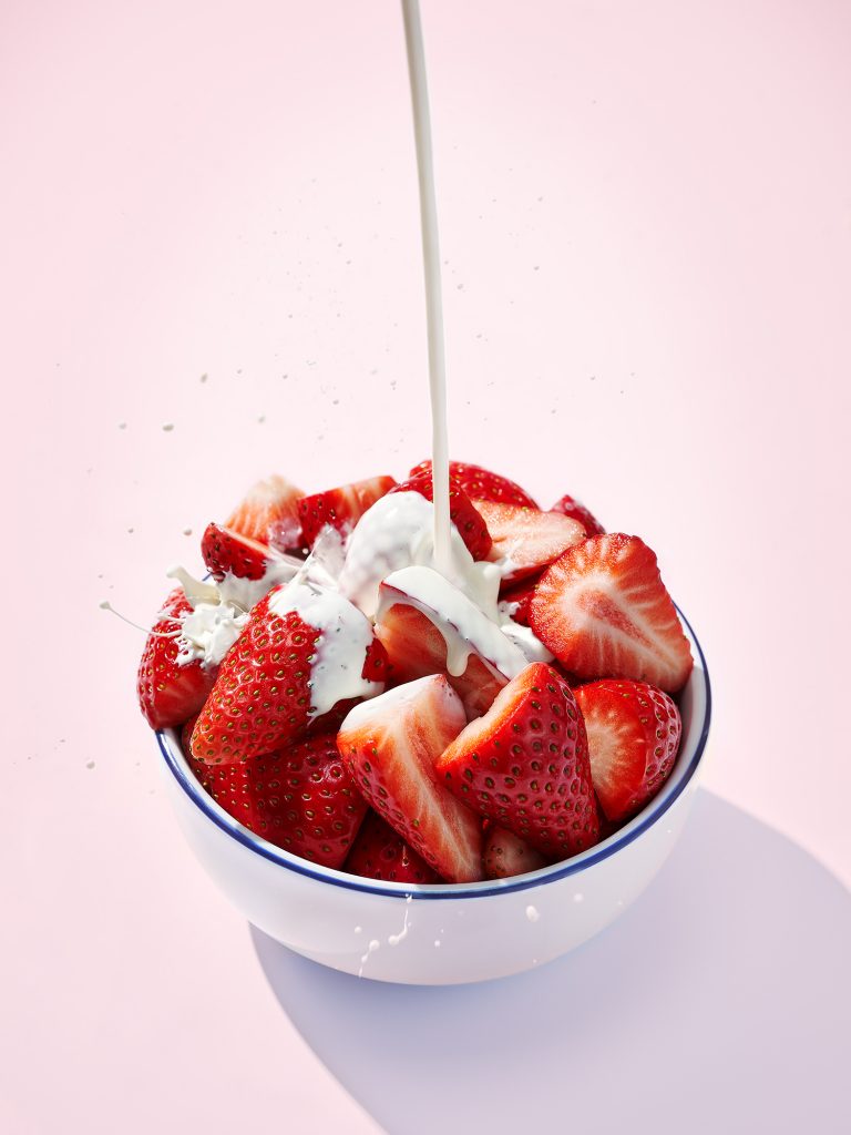 strawberries in a bowl with cream pouring and splashing